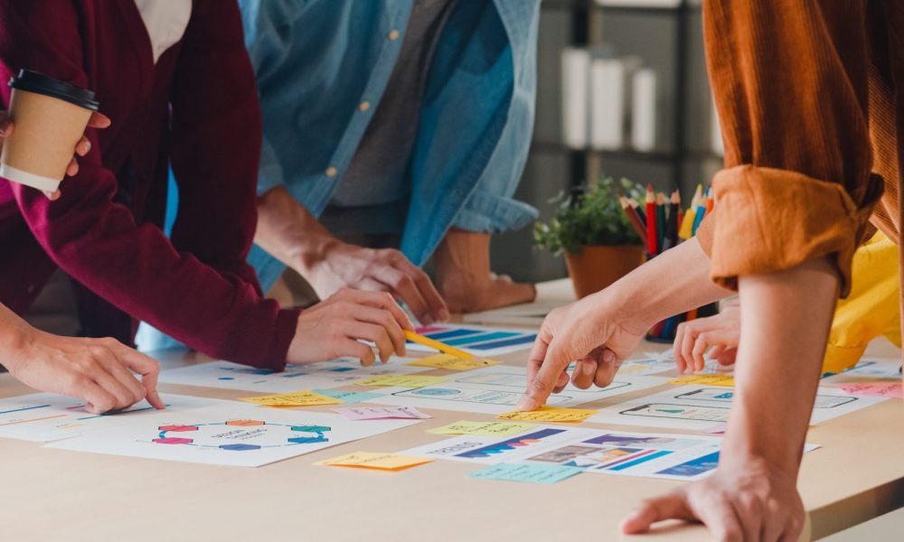 Asian businessmen and businesswomen meeting brainstorming ideas about creative web design planning application and developing template layout for mobile phone project working together in small office.